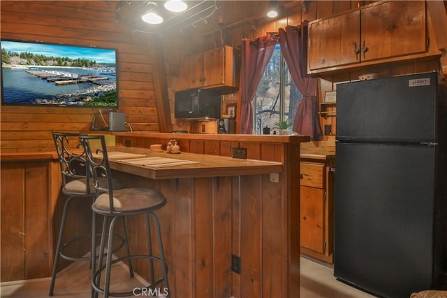 kitchen with wood counters, a kitchen breakfast bar, wood walls, and black appliances