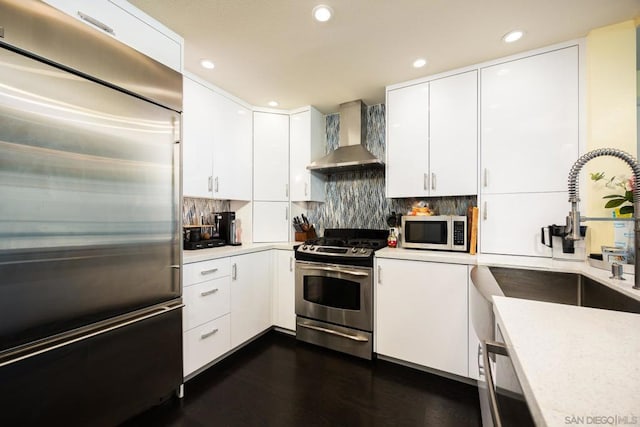 kitchen with stainless steel appliances, wall chimney range hood, dark hardwood / wood-style floors, backsplash, and white cabinets