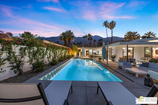 pool at dusk with a mountain view, an outdoor living space, and a patio