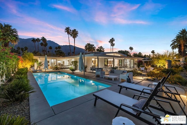 pool at dusk featuring outdoor lounge area, a mountain view, and a patio area