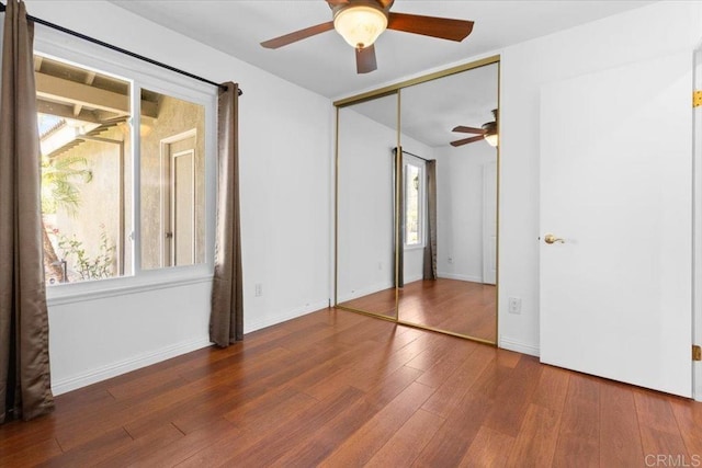 unfurnished bedroom featuring ceiling fan, a closet, dark hardwood / wood-style flooring, and multiple windows