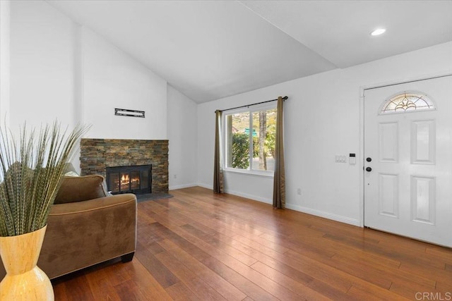 foyer entrance with a stone fireplace, wood-type flooring, and vaulted ceiling