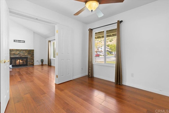 unfurnished living room featuring hardwood / wood-style floors, ceiling fan, a stone fireplace, and lofted ceiling