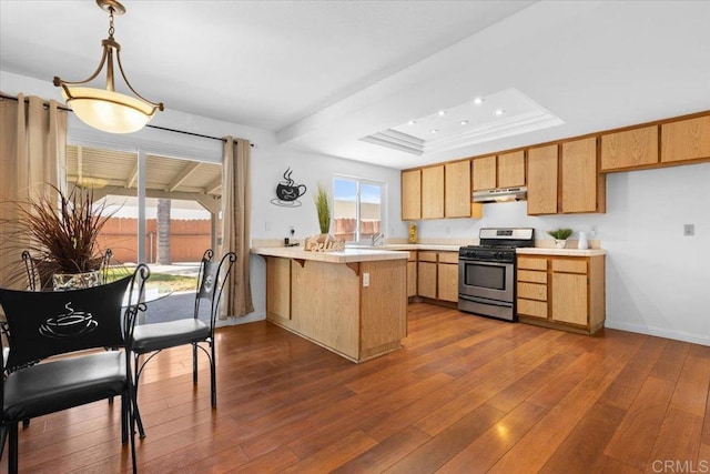 kitchen with a raised ceiling, dark hardwood / wood-style flooring, kitchen peninsula, pendant lighting, and stainless steel range with gas stovetop