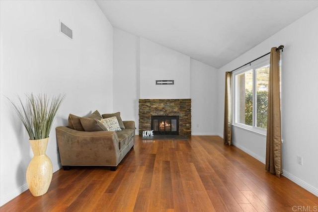 living room with a stone fireplace, dark wood-type flooring, and vaulted ceiling