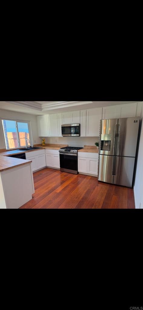 kitchen with sink, white cabinetry, dark hardwood / wood-style flooring, stainless steel appliances, and a high ceiling