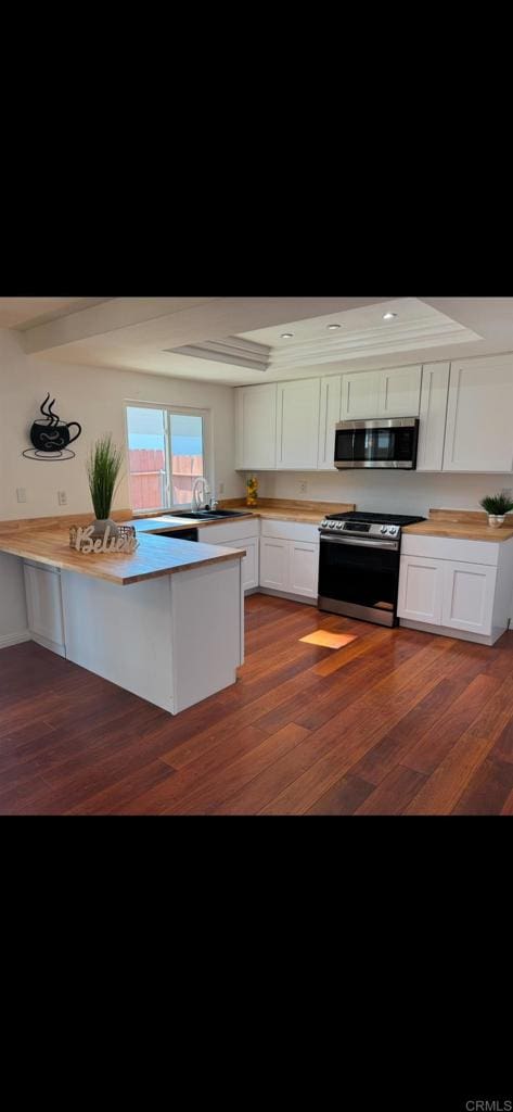 kitchen with white cabinetry, a kitchen breakfast bar, stainless steel appliances, dark hardwood / wood-style flooring, and kitchen peninsula