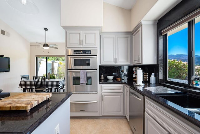 kitchen with ceiling fan, sink, dark stone counters, decorative backsplash, and stainless steel appliances