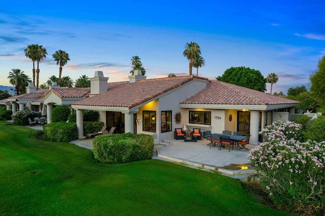 back house at dusk featuring a patio area, a lawn, and an outdoor hangout area