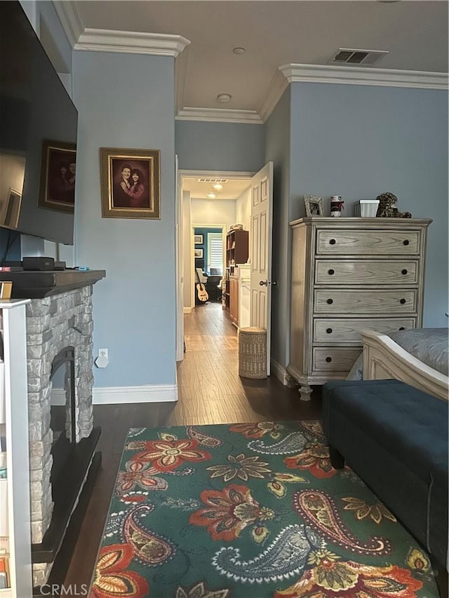 bedroom featuring crown molding, dark wood-type flooring, and a stone fireplace