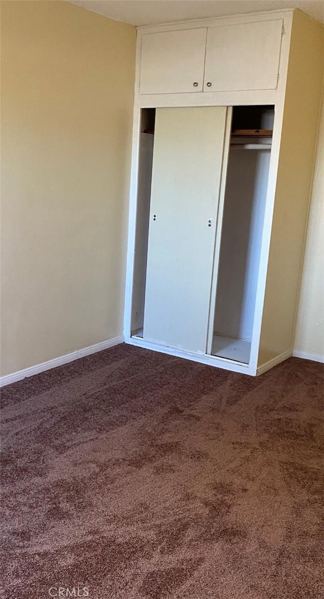 unfurnished bedroom with dark colored carpet and a closet