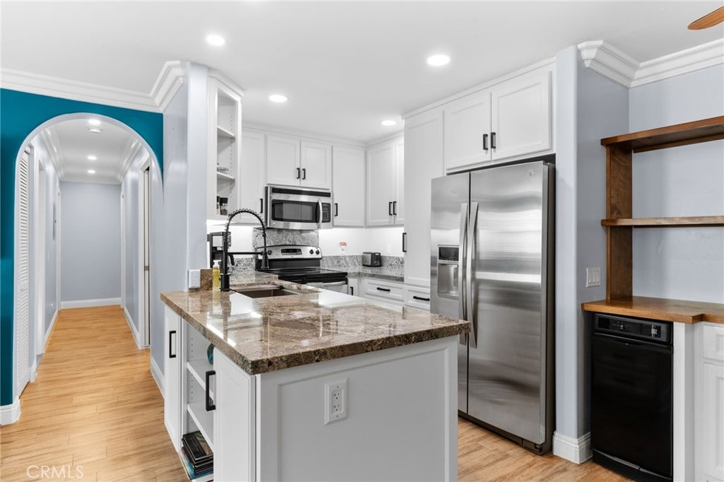 kitchen featuring stainless steel appliances, dark stone counters, light wood-type flooring, white cabinets, and ornamental molding