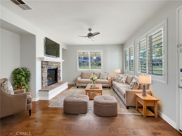 living room featuring ceiling fan, a stone fireplace, and wood-type flooring