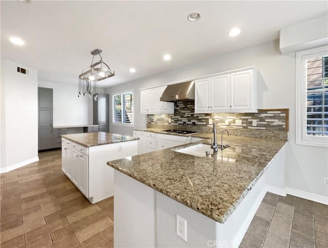 kitchen featuring a center island, wall chimney exhaust hood, kitchen peninsula, pendant lighting, and white cabinets