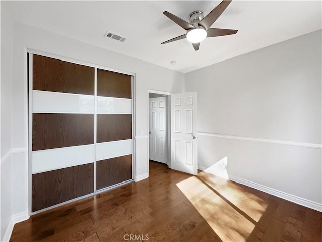 unfurnished bedroom with ceiling fan, dark wood-type flooring, and a closet