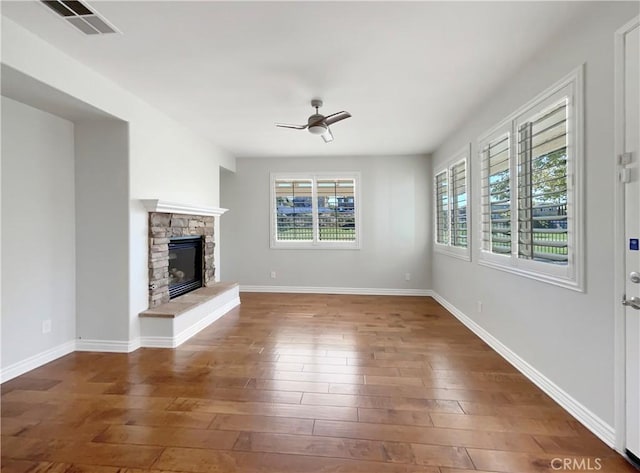 unfurnished living room featuring a stone fireplace, ceiling fan, and dark wood-type flooring