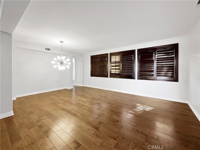 empty room with wood-type flooring and a notable chandelier