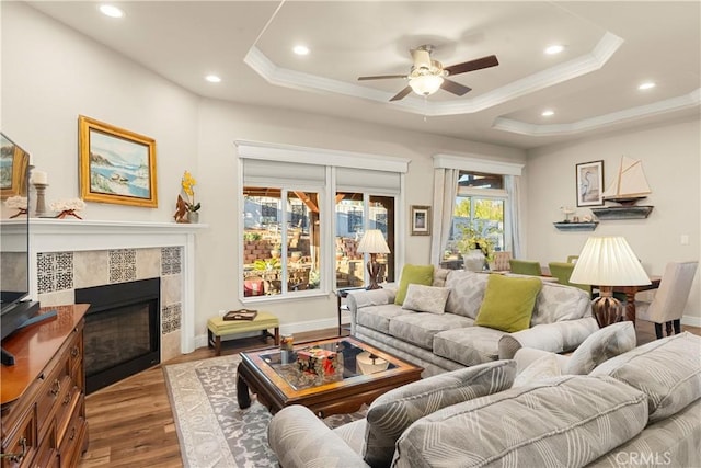 living room with hardwood / wood-style floors, a tray ceiling, crown molding, and a tiled fireplace