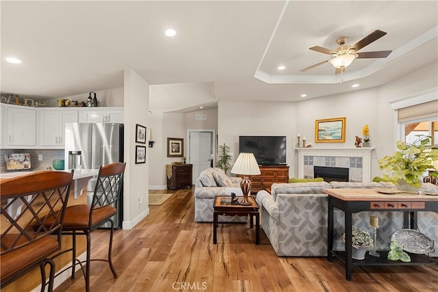 living room featuring a fireplace, ornamental molding, light wood-type flooring, ceiling fan, and a tray ceiling