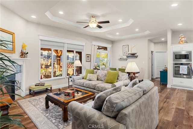 living room featuring hardwood / wood-style flooring, crown molding, a raised ceiling, and ceiling fan