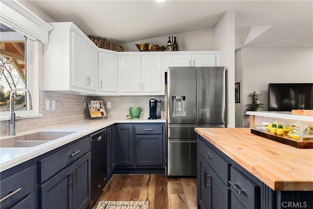 kitchen with vaulted ceiling, butcher block countertops, sink, white cabinets, and stainless steel fridge