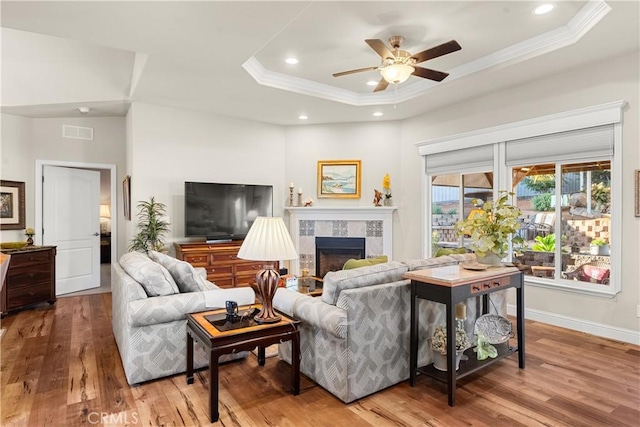 living room with a tray ceiling, crown molding, and a tiled fireplace