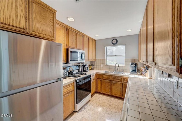 kitchen with backsplash, sink, tile counters, and appliances with stainless steel finishes