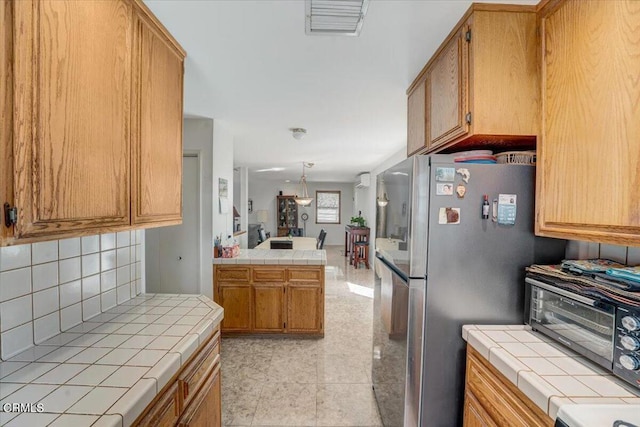 kitchen with tile countertops, light tile patterned floors, stainless steel refrigerator, and tasteful backsplash