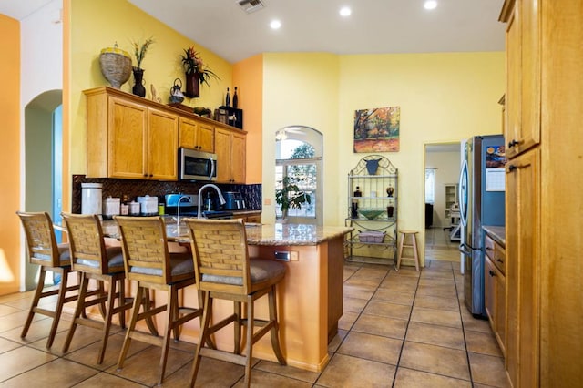 kitchen with a kitchen bar, a towering ceiling, backsplash, stainless steel appliances, and tile patterned flooring