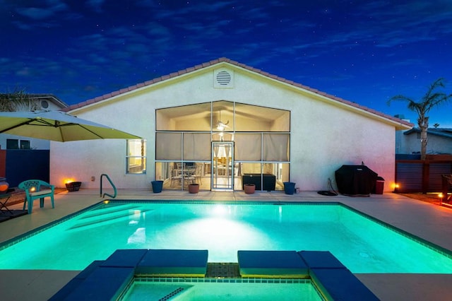 pool at night featuring an in ground hot tub, a patio, and area for grilling