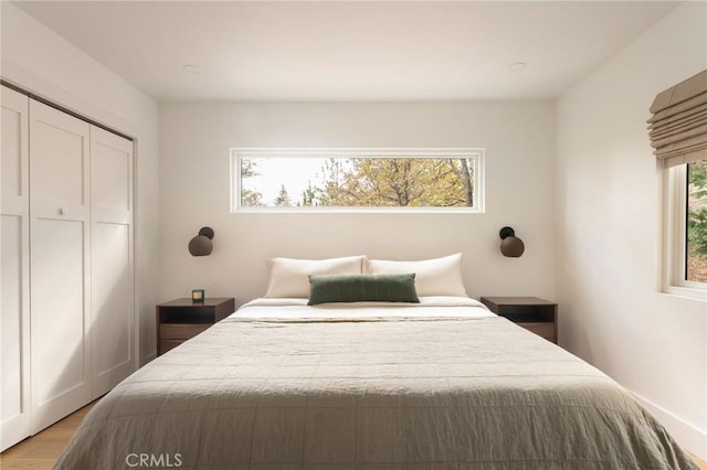 bedroom with a closet, light hardwood / wood-style flooring, and multiple windows