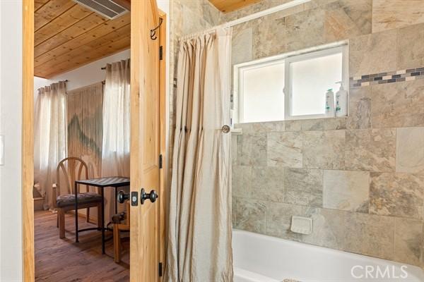 bathroom featuring hardwood / wood-style flooring, shower / bath combo with shower curtain, and wood ceiling