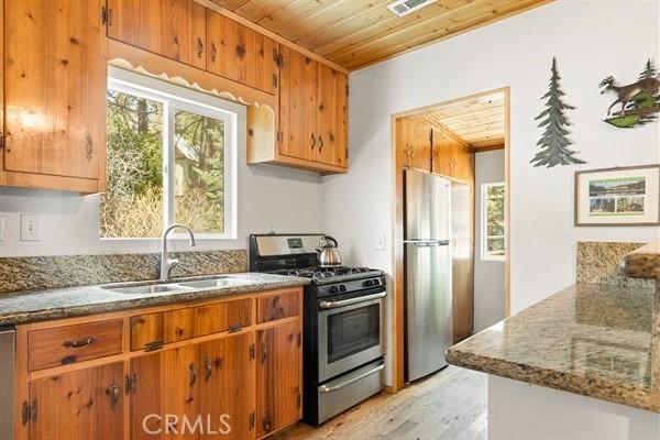 kitchen with sink, light hardwood / wood-style flooring, appliances with stainless steel finishes, light stone counters, and wood ceiling