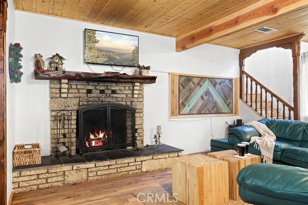 33544 Green Valley Lake Rd, Green Valley Lake, CA 92341 - living room featuring wood ceiling with exposed beams, a brick fireplace, wood finished floors, and stairway