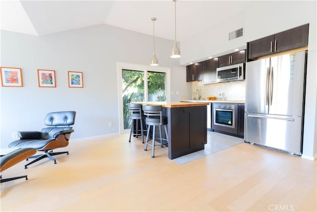 kitchen featuring hanging light fixtures, stainless steel appliances, light hardwood / wood-style flooring, vaulted ceiling, and a breakfast bar