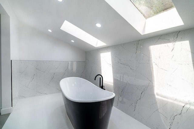 bathroom featuring a skylight, a bath, and tile walls