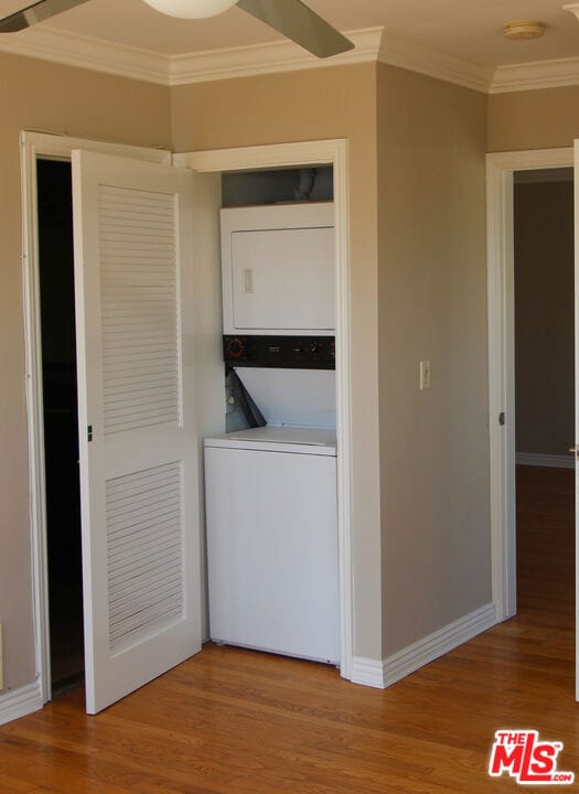 clothes washing area featuring ornamental molding, stacked washer / drying machine, and hardwood / wood-style flooring