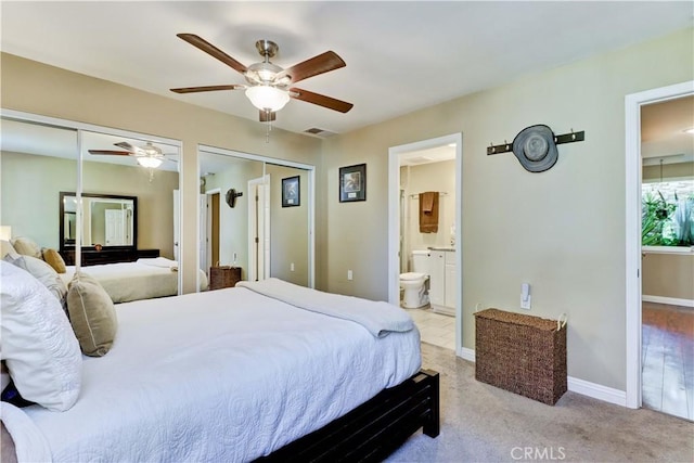 bedroom with connected bathroom, light carpet, two closets, and ceiling fan