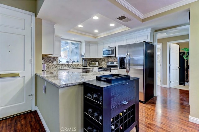 kitchen featuring appliances with stainless steel finishes, white cabinetry, hardwood / wood-style flooring, and a tray ceiling