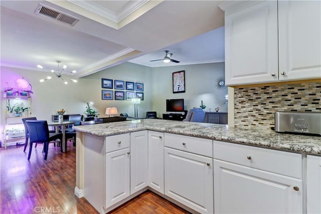 kitchen with white cabinets, tasteful backsplash, kitchen peninsula, ceiling fan with notable chandelier, and dark hardwood / wood-style flooring