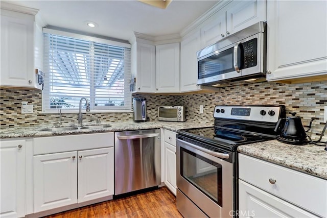 kitchen with light stone counters, stainless steel appliances, backsplash, white cabinets, and sink