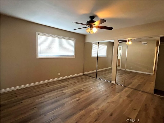 unfurnished bedroom featuring multiple windows, ceiling fan, two closets, and dark hardwood / wood-style flooring