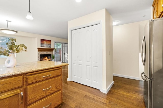 kitchen featuring dark hardwood / wood-style floors, stainless steel fridge, hanging light fixtures, a tiled fireplace, and light stone counters