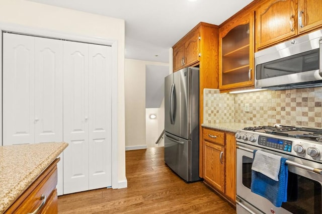 kitchen featuring tasteful backsplash, light stone countertops, appliances with stainless steel finishes, and light hardwood / wood-style floors