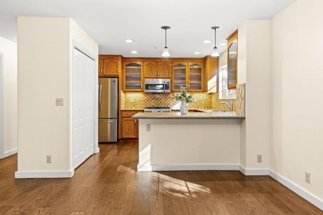 kitchen with appliances with stainless steel finishes, kitchen peninsula, hanging light fixtures, and backsplash