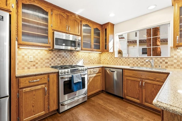 kitchen with sink, stainless steel appliances, light stone counters, wood-type flooring, and decorative backsplash