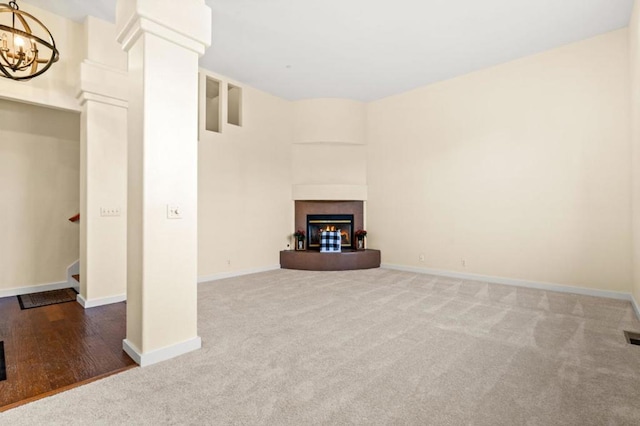 unfurnished living room with dark carpet, a tile fireplace, decorative columns, and a chandelier