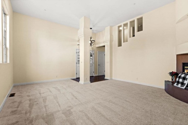 unfurnished living room with a towering ceiling, ornate columns, and carpet