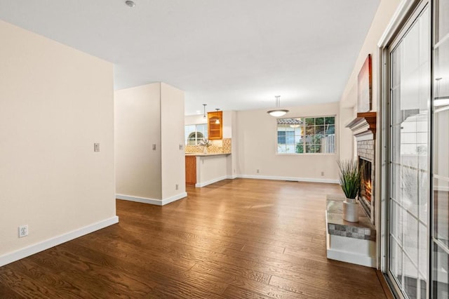 unfurnished living room featuring a brick fireplace and dark wood-type flooring