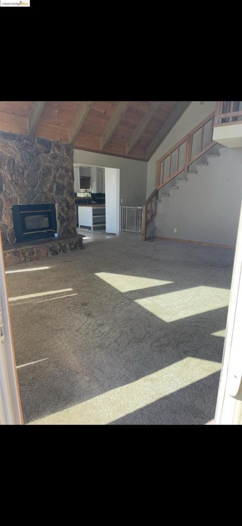 unfurnished living room with carpet, lofted ceiling with beams, a stone fireplace, and wood ceiling